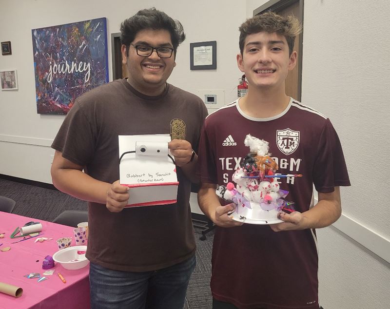 Two young men pose with small sculptures made from trash and craft items