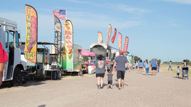 Rows of food trucks. Two adults with a small child walk past