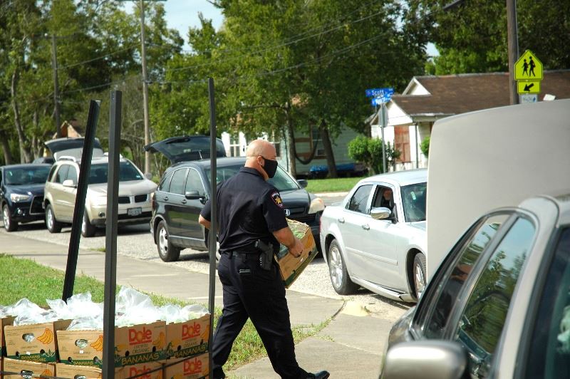 Man in police uniform carries food to line of vehicles