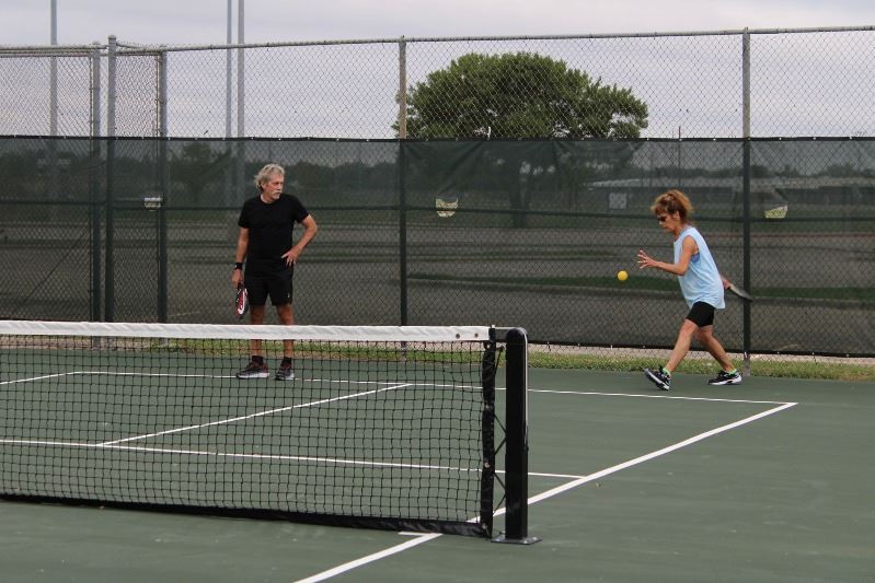 Man watches woman who is about to hit the ball during a game of pickleball.