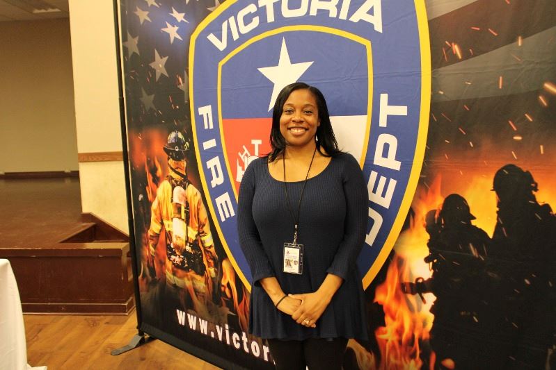 Smiling woman stands in front of Victoria Fire Department backdrop