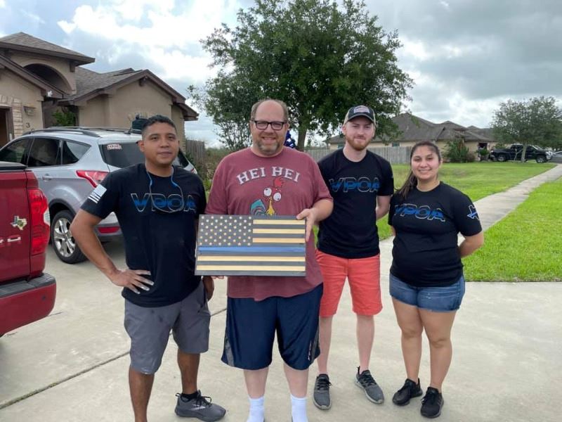 Four people pose for photo. Three have VPOA T-shirts. One holds a wood replica thin blue line flag.