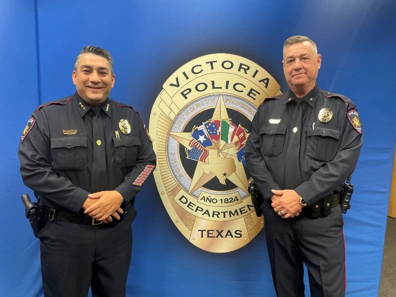 Two men in police uniform pose in front of a Victoria Police Department backdrop.