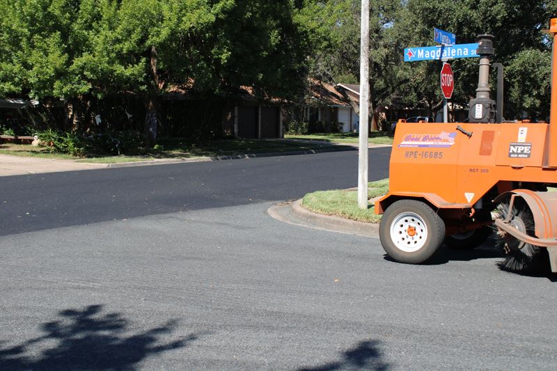 A small construction vehicle sits in a neighborhood on a gray road that intersects with a black road