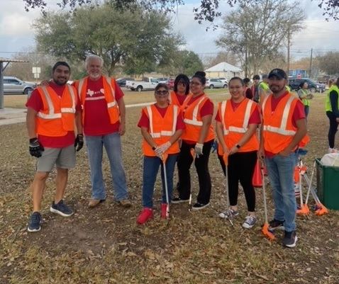 Small group of people in work vests and matching red shirts. Some hold trash grabbers.