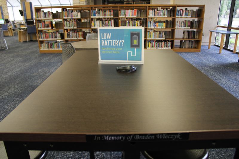 A table with an outlet and a sign that says Low Battery? Recharge your devices here.