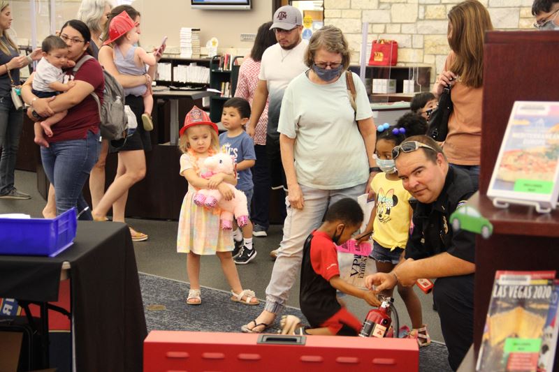 Children and families at the library. There is a fire department booth.
