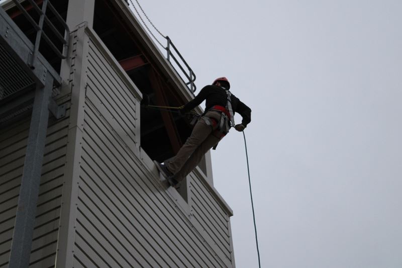 A person wearing a helmet rappels down the side of a building